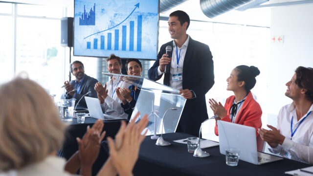 Rear view of diverse Audience applauding while male speaker speaks in a business seminar. International diverse corporate business partnership concept
