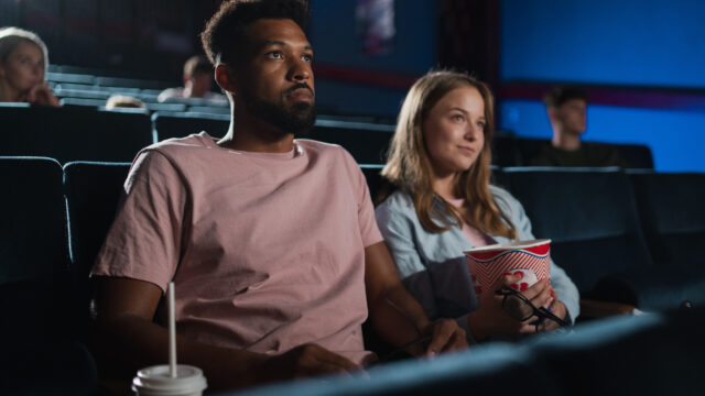 Cheerful young couple with popcorn in the cinema, watching film.