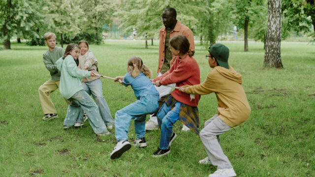 Diverse Group of Children Playing Tug of War with Male Teacher in Park