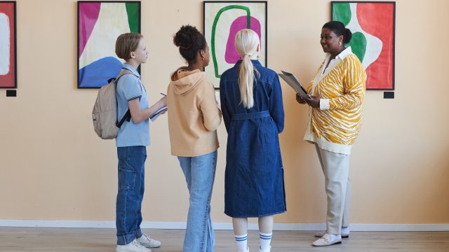 Group of teenagers listening to female teacher in modern art gallery