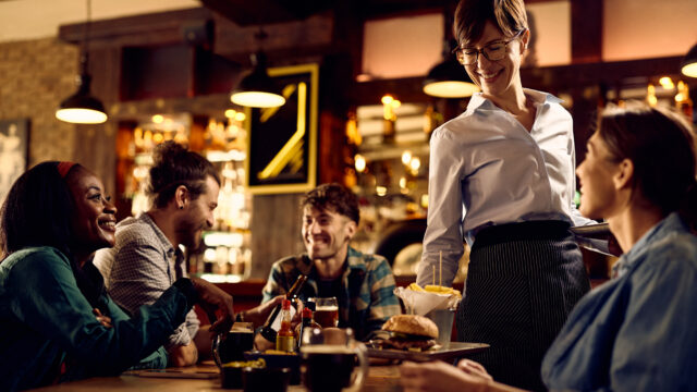 Happy waitress serving burgers and French fries to her customer in a bar.