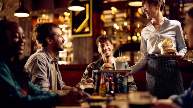 Happy waitress serving food to group of guests in a pub.