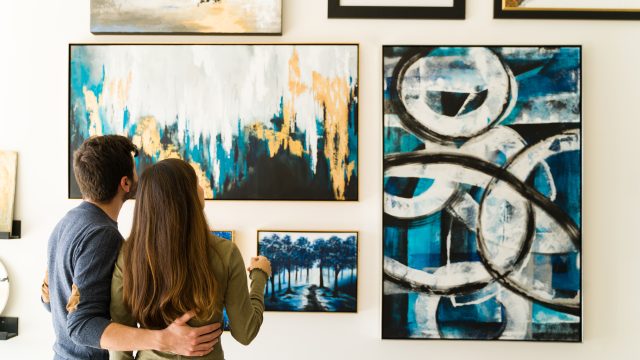 Rear view of a young woman and guy admiring the paintings of an art exhibition