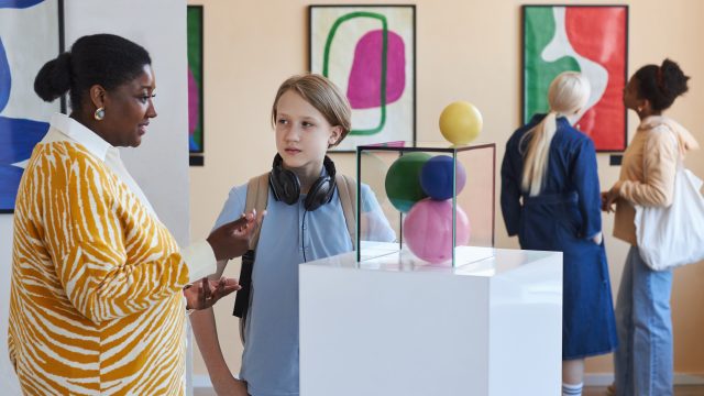 Young black woman explaining modern art to teenagers in museum